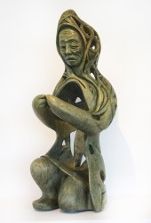 Carved in green Brazilian soapstone flecked lightly in black, brown and white, the figure of an elderly hooded woman genuflects.