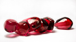 Clustered and sensuous oblong forms in translucent red glass have a smooth polished surface like the fruit that surrounds pomegranate seeds. Image 2