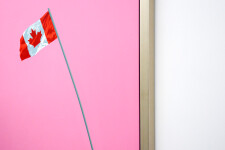 A Canadian flag flies smartly from the top of a grey-green pole that swoops into the centre of a flat, taffy pink sky. Image 5