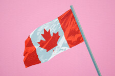 A Canadian flag flies smartly from the top of a grey-green pole that swoops into the centre of a flat, taffy pink sky. Image 2