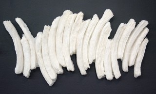 Long wafers of warm white glass frit are layered and stacked in a curated wall relief by Cheryl Wilson Smith.