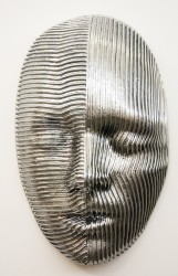 A large, striped mask in polished aluminum is set in a quiet expression in this sculpture by Dale Dunning.