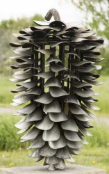 Four feet tall, stainless steel pine cone is set vertically on a block of stone.