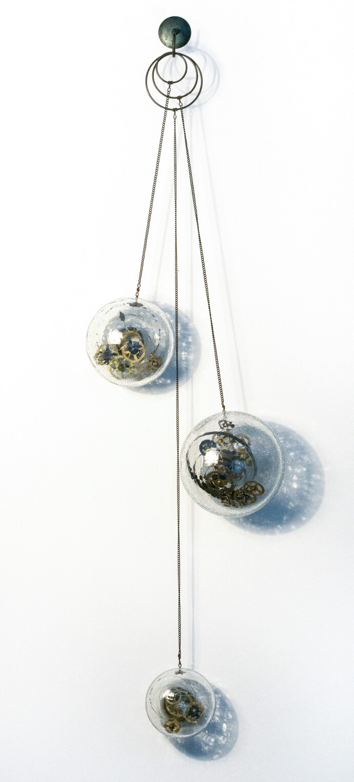Three blown glass orbs that contain assembled clock works, wheels, sprockets and coils, hang from fine chain in this unique wall sculpture.T…