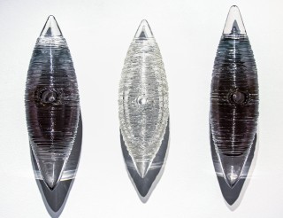 Three textured glass cocoon shapes in clear, charcoal grey and black are curated vertically in this unique wall sculpture by Julia Reimer.