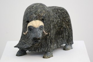 This finely carved muskox, its long fur being blow by the wind, includes carved horn set into the stone.