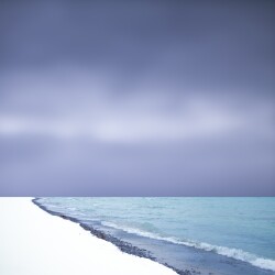 A moody sky looms large over turquoise waters and a bright white shore.