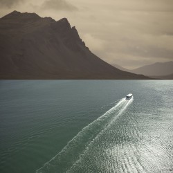 A ferry crosses a sunlit sea towards dark distant mountains in this stunning photographic print by Mark Bartkiw.