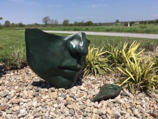In this outdoor sculpture by Marlene Hilton Moore, the lower half of a face in a green patinated bronze is set at an angle on the ground.