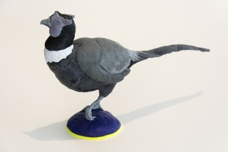 Cast in resin, a figurine of a pheasant posed on an indigo base points to a theme of human and animal interaction.
