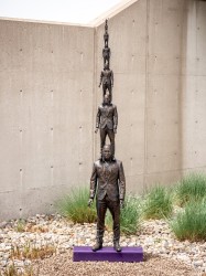 Seven bronze suited men in diminishing size are stacked in this intriguing outdoor sculpture by P.