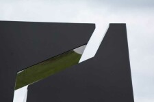 A rectangular, steel outdoor sculpture in black is divided in three parts, like a puzzle, the edges polished and reflective. Image 5