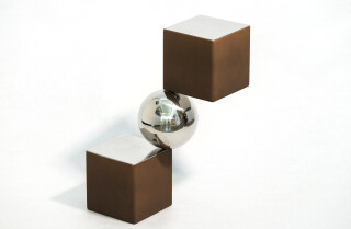 A polished aluminum sphere sits artfully balanced between two rust-coloured and silver cubes in this dynamic modern tabletop sculpture by Ph…