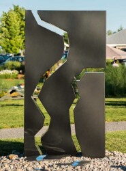 A rectangular, steel outdoor sculpture in black is divided in three parts, like a puzzle, the edges polished and reflective.