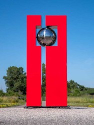 A polished stainless steel ball is framed by rectangular cardinal red forms in this outdoor sculpture by French artist Philippe Pallafray.