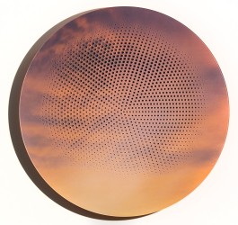 A black and white pigment print of the sun rising through clouds is perforated with a brilliant orange geometric design in this tondo by Rya…