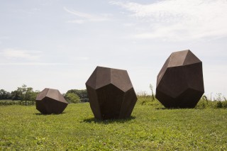 This large scale outdoor installation consists of three hollow, polygonal steel boulders called Drop Stones that have a rusted, weathered pa…