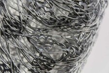 A continuous strand of slender, silver aircraft cable is threaded through polished squares of stainless steel to create an ethereal mask. Image 6