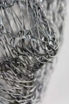 A continuous strand of slender, silver aircraft cable is threaded through polished squares of stainless steel to create an ethereal mask. Image 4