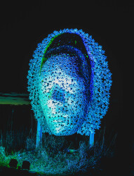 This contemporary wall sculpture of a mask is made out of metal.