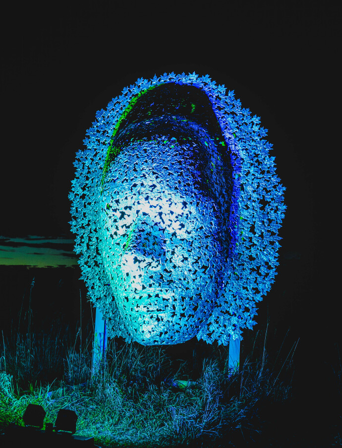 This contemporary wall sculpture of a mask is made out of metal.