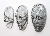 Narrow strips of aluminum are skillfully shaped in to the curves and folds of three masks in this triptych by sculptor Dale Dunning. Image 3