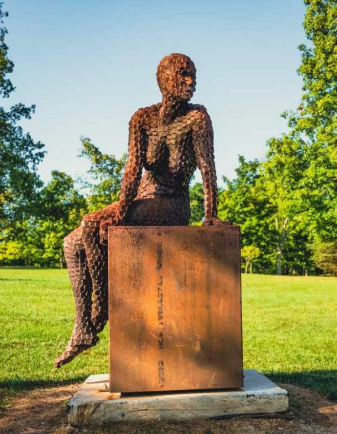 A seated female figure strikes a casual pose, body half turned in this imposing sculpture by American artist, Jason Kimes.