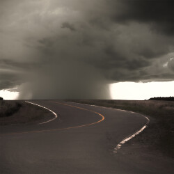 This contemporary photograph of storm clouds in a country landscape is in black and white.