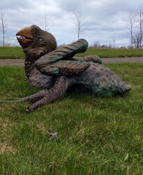 Toronto artist, Nicholas Crombach’s large, bronze outdoor sculpture of a baby macaw depicts the parrot struggling and screeching from an awk…