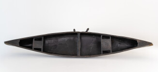 This indoor table top bronze sculpture features a man sitting on an overturned canoe. Image 5