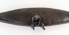 This indoor table top bronze sculpture features a man sitting on an overturned canoe. Image 9