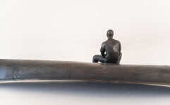 This indoor table top bronze sculpture features a man sitting on an overturned canoe. Image 12