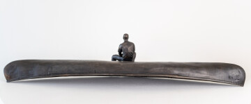 This indoor table top bronze sculpture features a man sitting on an overturned canoe. Image 3
