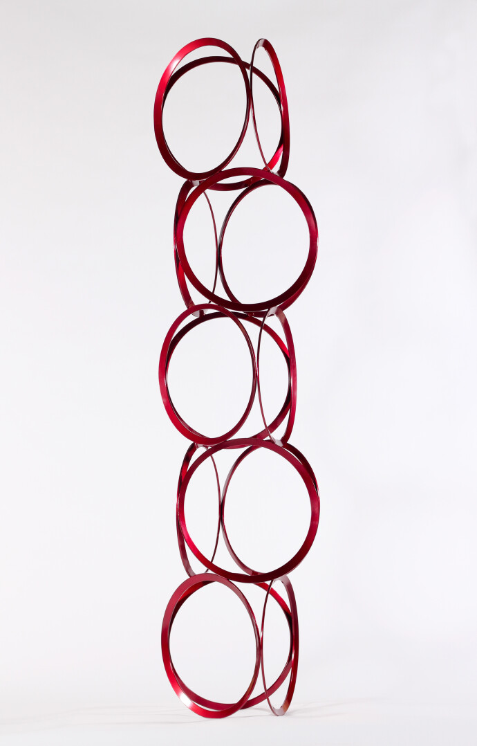 Slender rings of flattened candy red steel are stacked into an elegant yet playful column by master sculptor Shayne Dark.