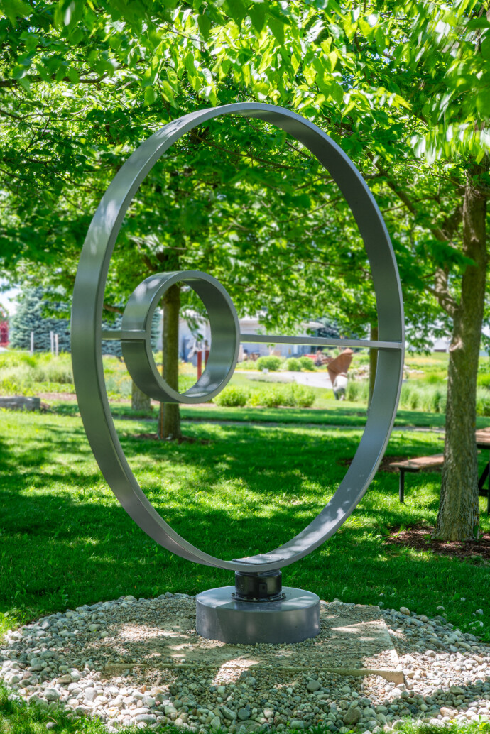 This contemporary outdoor kinetic sculpture is forged from steel into a circle.